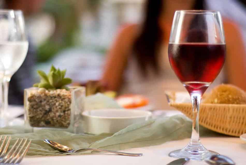 Glass of red wine on a table with silver cutlery, a bread basket and a small decorative succulent plant.