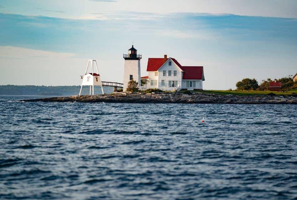 Lighthouse and keeper's abode on stone shoreline in midst of rippling blue water.