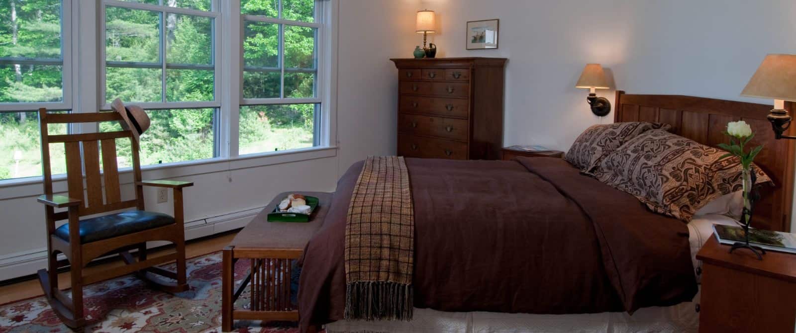 Bedroom with craftsman-style furniture, bed made up in cozy brown comforter with a colorful rug on wooden floor.