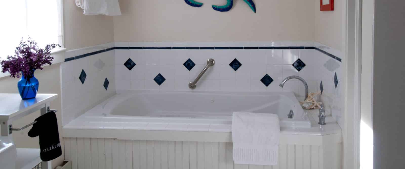 Jetted bathtub with tile surround in a bright white bathroom with blue accents.