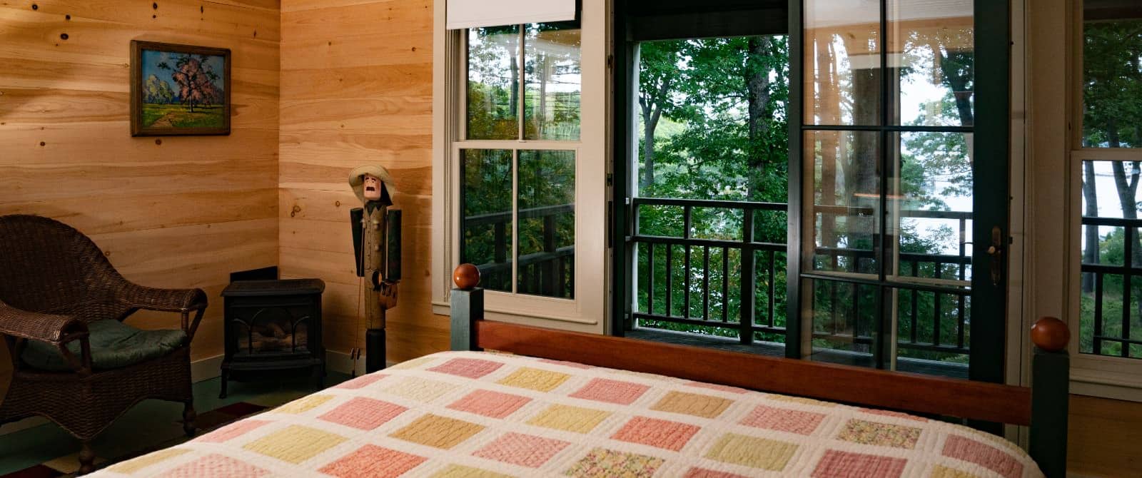 Cozy bedroom with wooden paneling, doors leading to patio and a bed made up with a pretty pastel quilt.