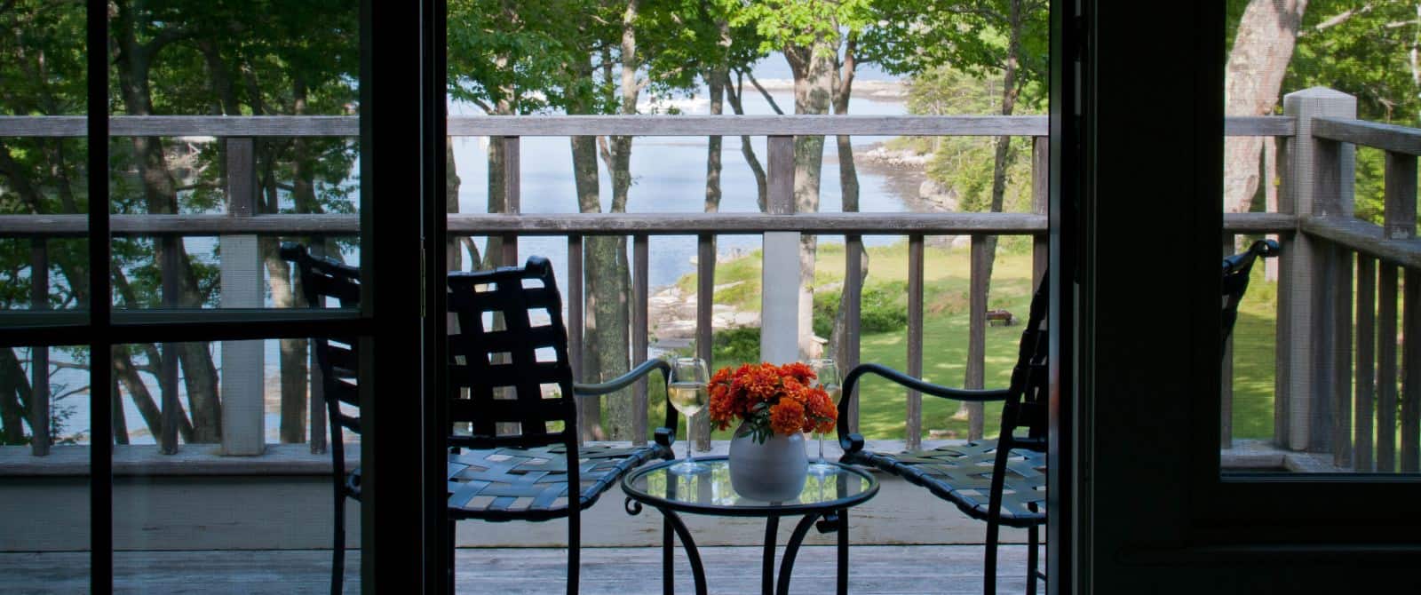 View of patio with two chairs and a small glass-top table from inside wooden framed patio doors.