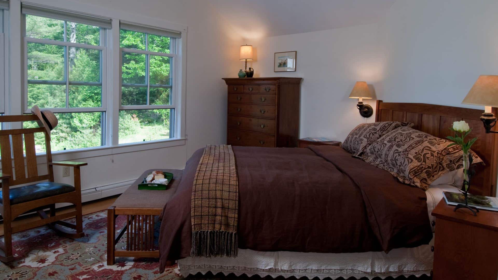 Bedroom with craftsman-style furniture, bed made up in cozy brown comforter with a colorful rug on wooden floor.