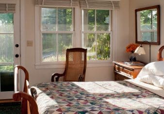 Sun falls lightly through large windows onto a wooden sleigh bed made up with a pretty quilt.