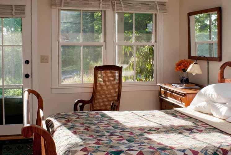 Sun falls lightly through large windows onto a wooden sleigh bed made up with a pretty quilt.