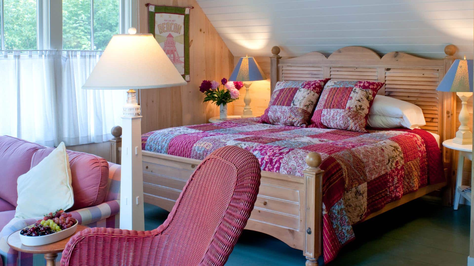 Pretty bedroom decorated in pinks and greens, with a sloped ceiling and large wooden bed.