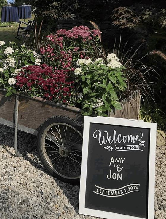 Garden cart full of flowers and plants next to a chalkboard sign reading, 